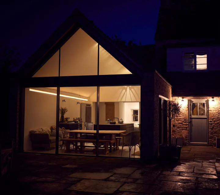 A glazed gable home extension by Total Building North West, lit at dusk